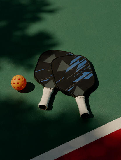 Deux raquettes de pickleball et une balle orange sur un court vert à Amanyara, resort aux Turks-et-Caïques.