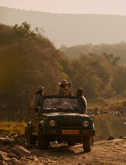 Safari vehicle on a dusty track at Aman-i-Khas, with forested hills in the hazy distance.