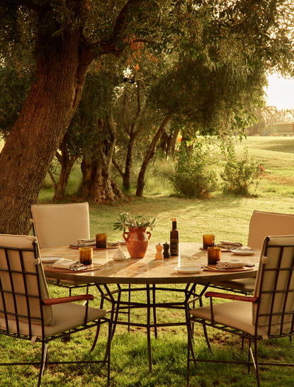 Tavolo da pranzo all'aperto sotto gli alberi ad Amanjena resort, con sedie e paesaggio verdeggiante.