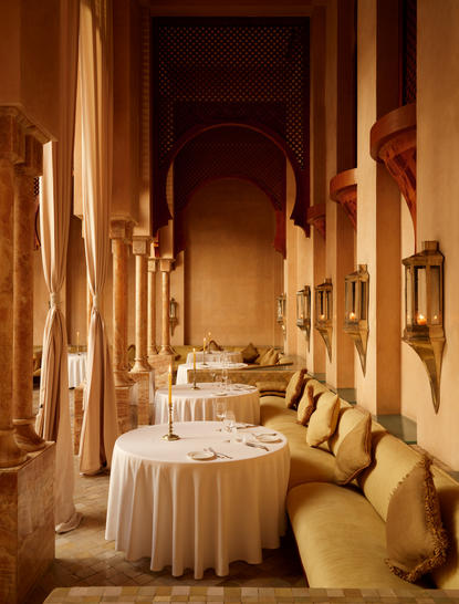 Moroccan dining room at Amanjena with warm-lit archway, yellow cushioned seating, and cream tablecloth.