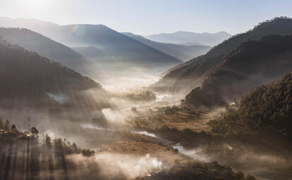 Misty mountain valley at Aman Bhutan with forested slopes and morning light filtering through clouds.
