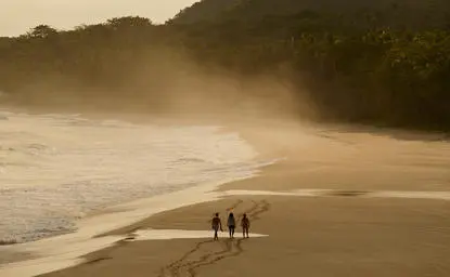 Surfers standing on golden sand at Amanera resort, with misty waves rolling onto the beach.