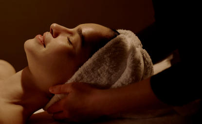 Woman receiving facial treatment at Aman New York spa, relaxing with eyes closed.