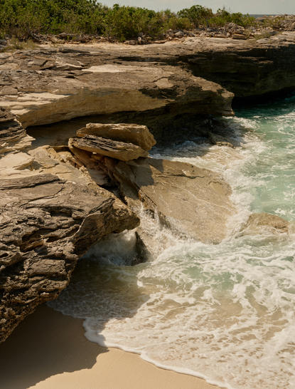 Turquoise waters lap a sandy beach bordered by weathered rock formations at Amanyara, Turks and Caicos.