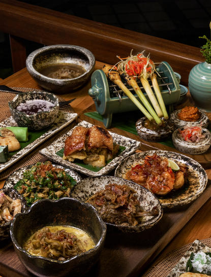 Jamuan Makan Nusantara dining spread at Amandari resort, featuring grilled meats, vegetables and traditional Indonesian dishes on wooden table.