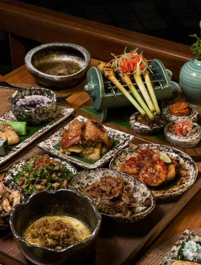 Jamuan Makan Nusantara dining spread at Amandari, featuring traditional Indonesian dishes with grilled meats, vegetables and condiments on wooden table.