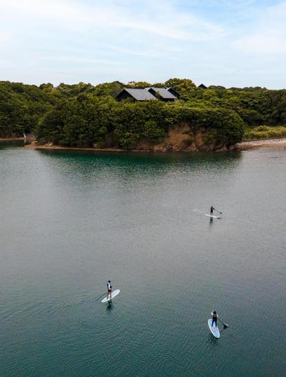 宾客在安缦伊沐度假村的海湾中划桨冲浪,清澈的绿松石色水域环绕着树木繁茂的岛屿。