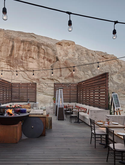 Dining venue at Amangiri resort with wooden tables and chairs on a terrace overlooking desert cliffs at dusk.