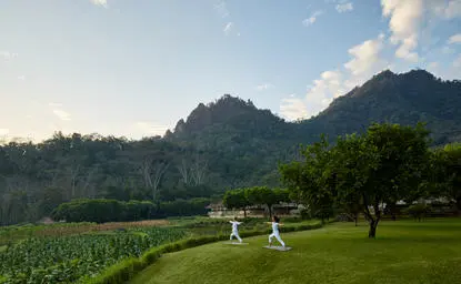 Yoga session on manicured lawn with volcanic mountains rising beyond at Amanjiwo resort.