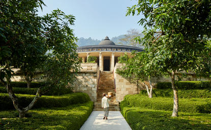 Amanjiwo's principal residence viewed through tree-lined gardens, with manicured lawns and a reflecting pool leading to the columned façade.