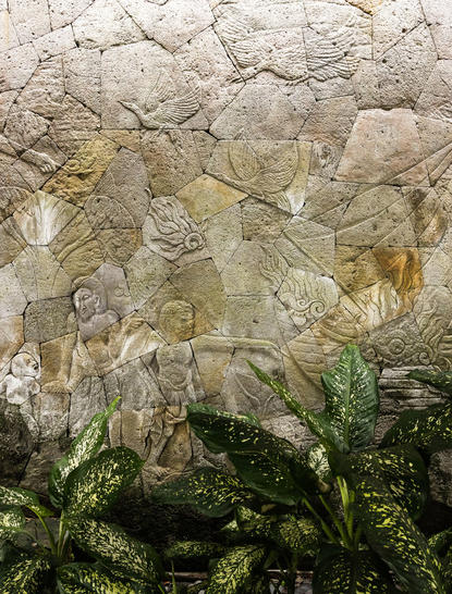 Intricate stone bar carvings at Amankila, Bali, with weathered surface and tropical plants below.