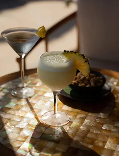 安缦丘澜度假村酒吧的两杯鸡尾酒，一杯清澈，一杯绿色，配以装饰配菜。