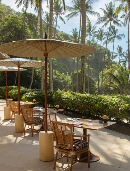 Amankila beach club terrace with timber parasol and dining chairs overlooking tropical gardens, Bali.