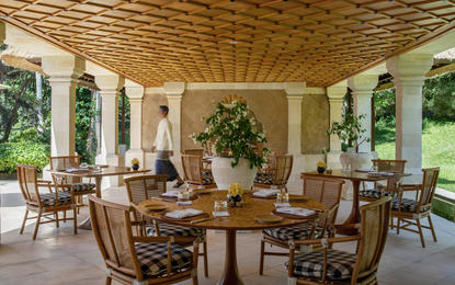 Amankila resort beach club restaurant with wooden ceiling, cream columns, and dining tables overlooking Bali gardens.