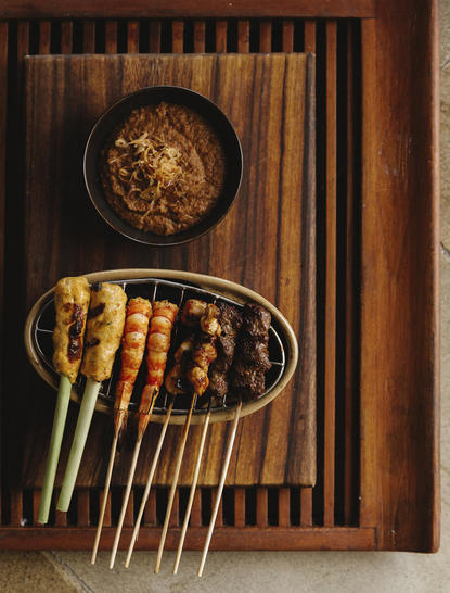 Satay skewers on a wooden grill at Amankila's restaurant in Bali, with peanut sauce on the side.