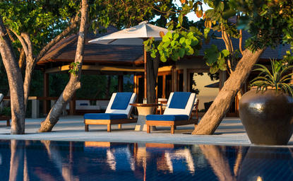 Amanpulo রিসর্টের পুল পাশে নীল সানলাউঞ্জার এবং গাছ।