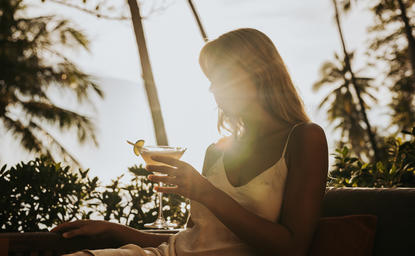Femme assise parmi les palmiers au resort Amanpuri, lumière dorée du jour.