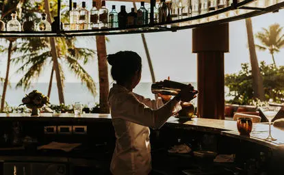 Silhouette of a person at a piano with tropical palms visible through windows at Amanpuri resort.