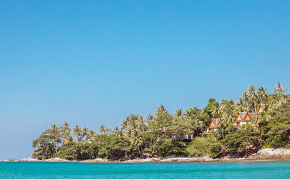 Amanpuri resort's forested coastline meets turquoise waters under clear skies.