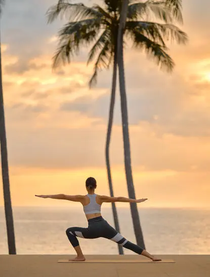 Person practising yoga on beach at sunset, with palm trees and sea at Amanpuri.