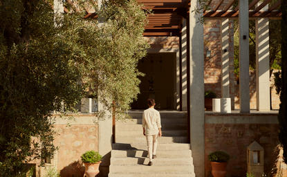 Arrival pathway at Amanruya with stone walls, olive trees, and warm sunlight filtering through the entrance.