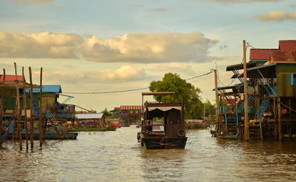 Sunset cruise on Tonlé Sap Lake with wooden boats passing traditional stilt village houses at Amansara, Cambodia.