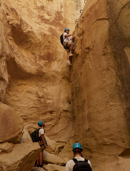 Climber scaling a red rock face during a via ferrata experience at Amangiri resort.