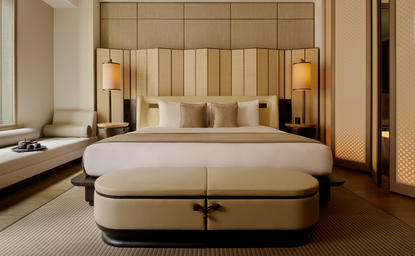 安缦纽约酒店初级套房卧室，设米色床铺和木质床头背景墙。