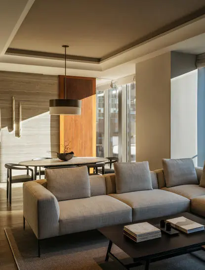 Aman New York living room with gray sofa, wooden cabinetry, and floor-to-ceiling windows overlooking the city.
