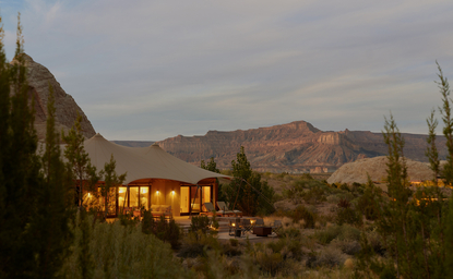Amangiri's stone pavilion glows at dusk beneath desert mountains and scattered conifers.