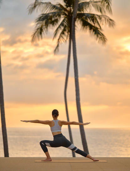 Femme pratiquant le yoga au coucher de soleil à la plage d'Amanpuri, station balnéaire en Thaïlande.