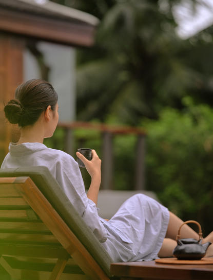 Woman in white linen resting on a green lounger at Amanpuri resort, Thailand.