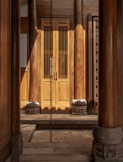 Antique wooden pavilion entrance at Amanyangyun, with ornate carved doors framing a golden-lit interior chamber.