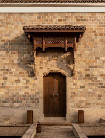 Wooden entrance door beneath a timber canopy at Amanyangyun Shanghai villa, set within a brick façade.