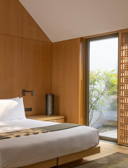 养云安缦度假村的明清风格卧室，木质墙面和宽敞床铺，落地窗外可见园林景观。