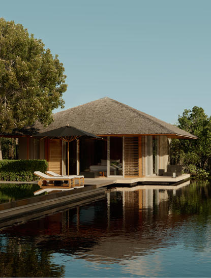アマンヤラ・リゾートの3ベッドルーム・トランクイリティ・ヴィラ、池に映る茅葺き屋根の建物と庭園。