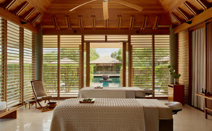 Wellness room at Amanyara resort with wooden vaulted ceiling, floor-to-ceiling windows overlooking tropical gardens, and a soaking tub.