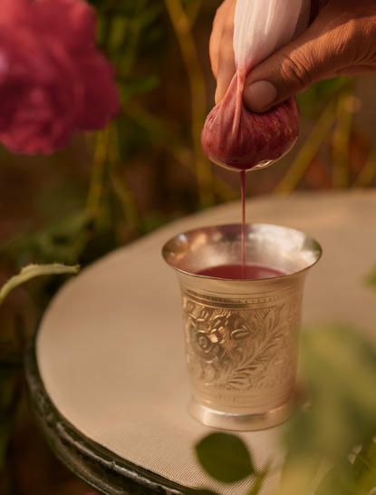 Hand pouring water into a glass at Aman-i-Khas, with roses in the background.