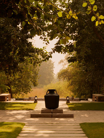 Sunlit pathway through tree-lined avenue at Aman-i-Khas, India, leading to a central water feature.