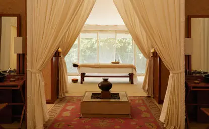 Spa interior at Aman-i-Khas with wooden treatment bed, flowing curtains and views across Indian landscape.