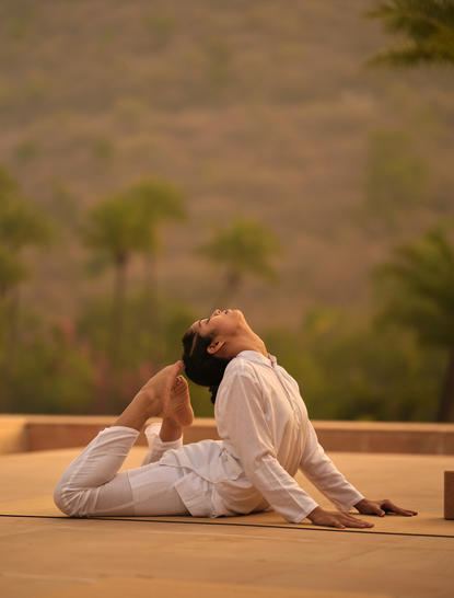 Woman in white practising yoga on a terrace at Amanbagh, with landscape views beyond.
