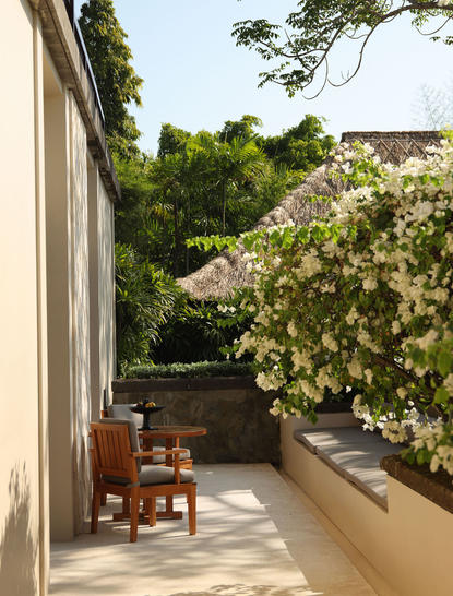 Resort swimming pool terrace at Aman Villas at Nusa Dua, Indonesia, with wooden lounger and lush greenery.