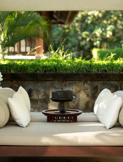 Outdoor seating area at Aman Villas at Nusa Dua with cream cushions, decorative pillows and black table nestled against lush greenery.