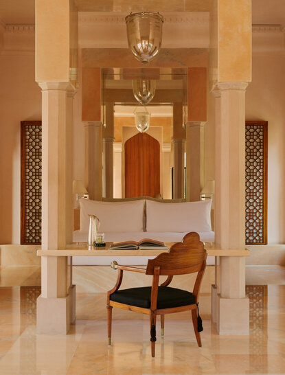 Terrace haveli suite bedroom at Amanbagh with arched doorways, carved wooden screens, and a chair overlooking the courtyard.