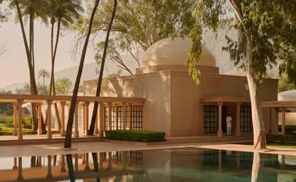 Amanbagh's main spa building reflected in a still pool, framed by palm trees at dusk.