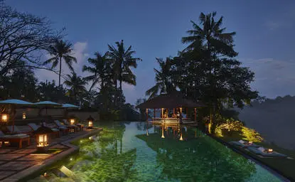 Golden pavilion and infinity pool at Amandari in Ubud, Bali, illuminated at dusk.