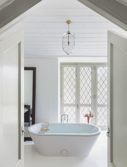 Bathroom at Amangalla with freestanding bath beneath latticed window and pendant light.