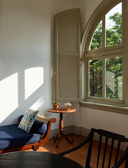 Sunlit corner of an Amangalla suite with arched window, wooden chair, and daybed.