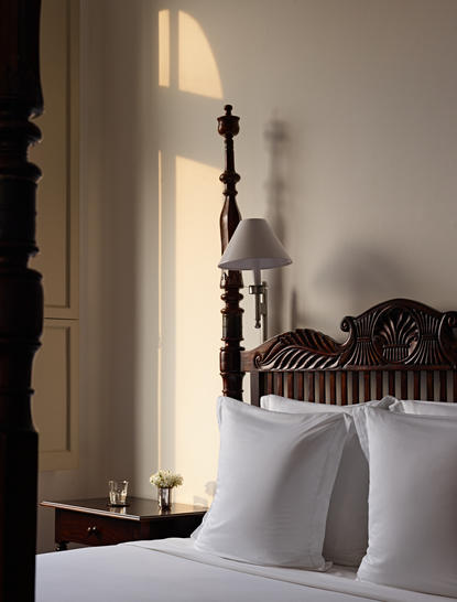 Sunlit principal bedroom at Amangalla with wooden headboard and white bedding, Sri Lanka.