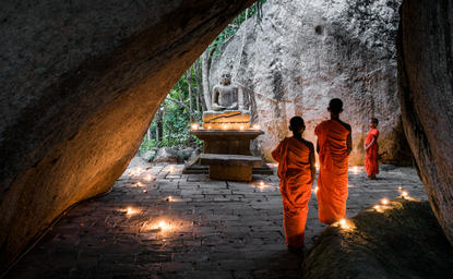 Buddhist monks in saffron robes walk through a candlelit stone passageway at Amangalla, Sri Lanka.